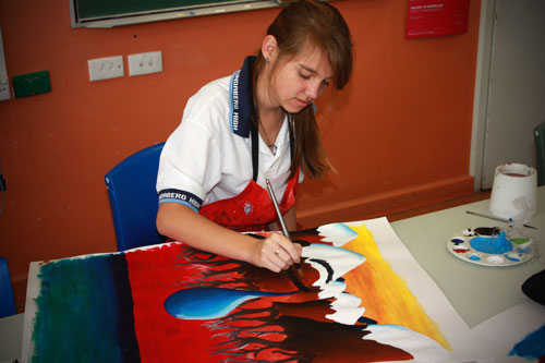 Female student sitting at table painting.