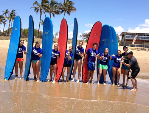 Students with surfboards standing in sea water.